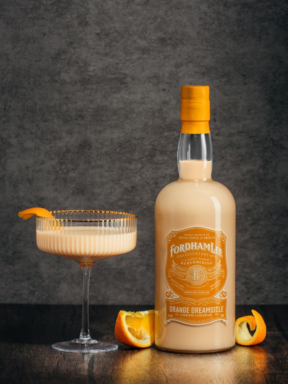 Fordham Lee Orange Dreamsicle Cream Liqueur Bottle With A Creamy Orange Cocktail, Garnished With A Fresh Orange Twist, Set On A Dark Wooden Surface.